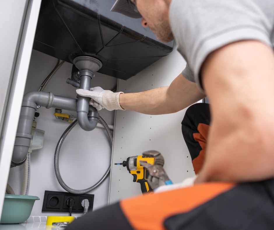Plumber working on pipes under a sink